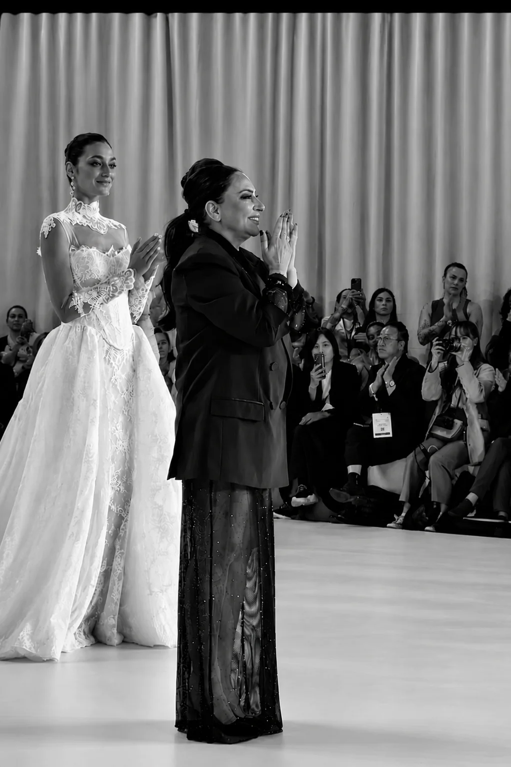 Silva Erkoç applaudiert am Ende ihrer Modenschau auf dem Laufsteg, neben ihr ein Model im Brautkleid aus Spitze